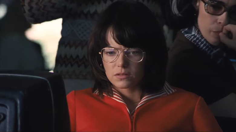 Stone with dark hair and glasses in red jacket