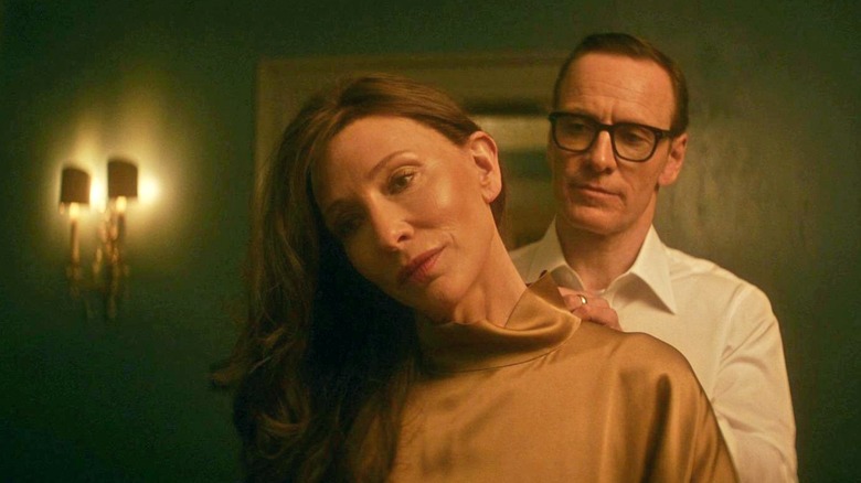 George clasps a necklace around the neck of Kathryn in a dimly-lit hallway in "Black Bag" (2025)