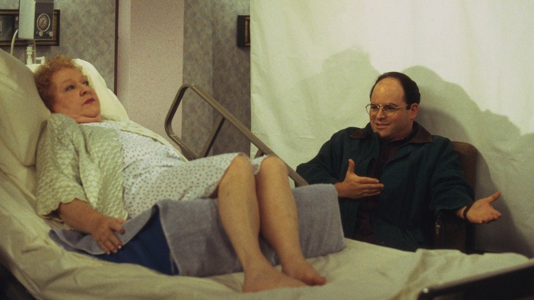Mrs. Costanza lies in hospital bed next to smiling George