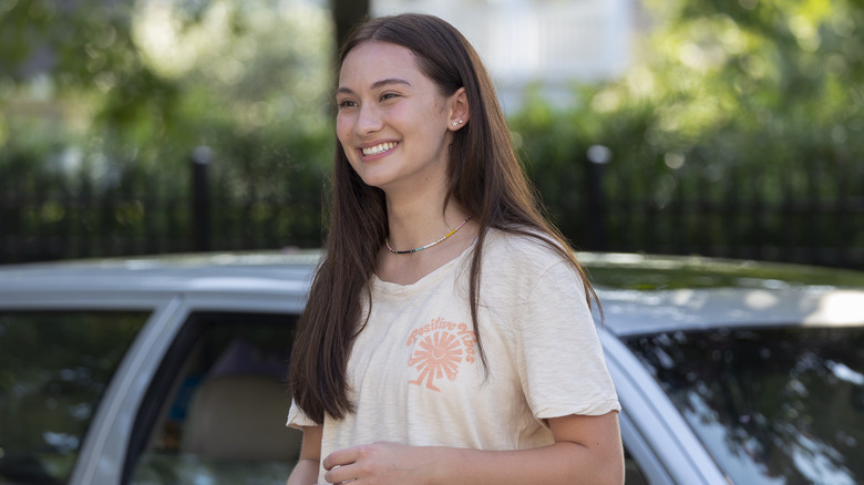 Belly smiling in front of a car in 