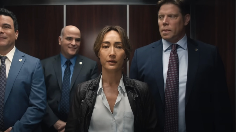 Ballard stands in an elevator surrounded by men in 