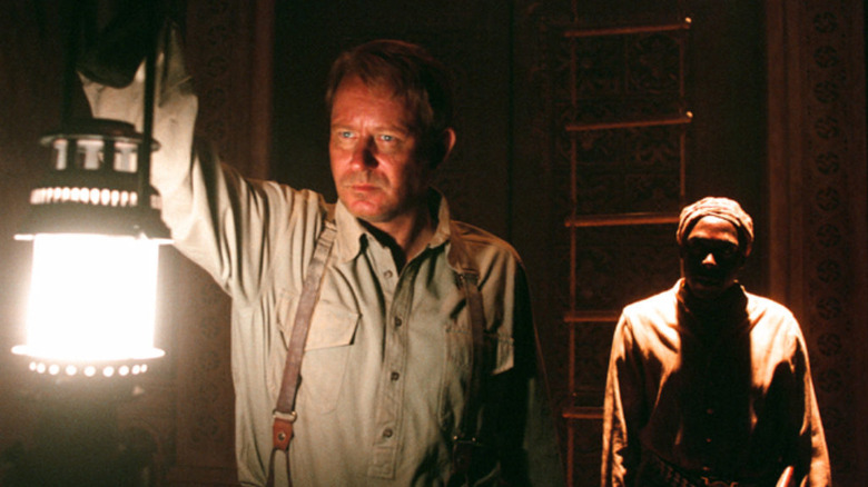 Merrin holds up a lantern in a dark chamber in The Exorcist: The Beginning