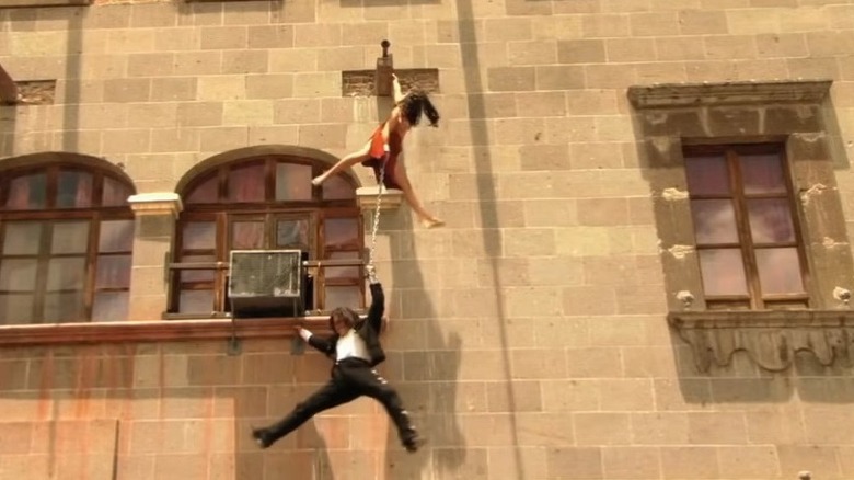 El Mariachi and Carolina swinging from the side of the building