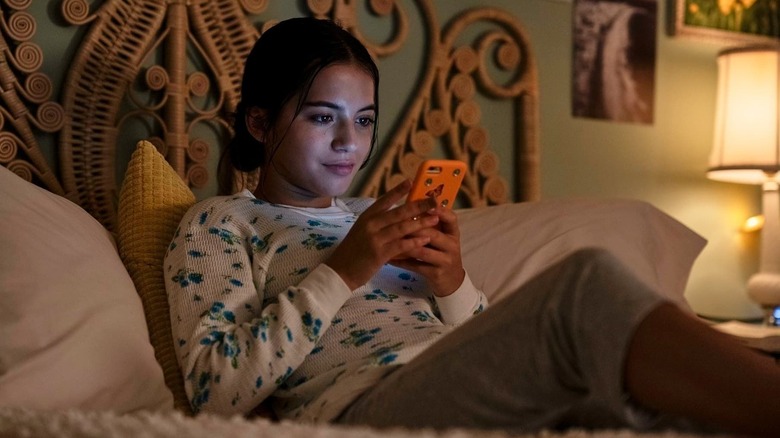 Aza smiling at her phone in "Turtles All the Way Down" (2024)