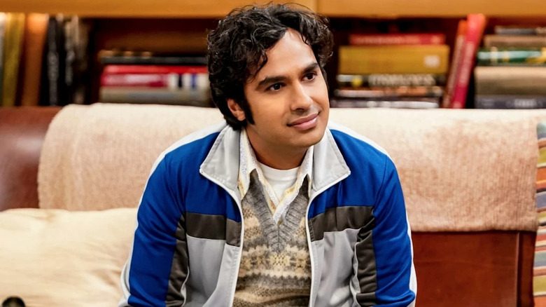 Raj on the couch half-smiling with curly hair on The Big Bang Theory
