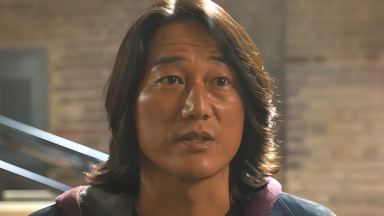 Han Lue stands in front of a car looking worried