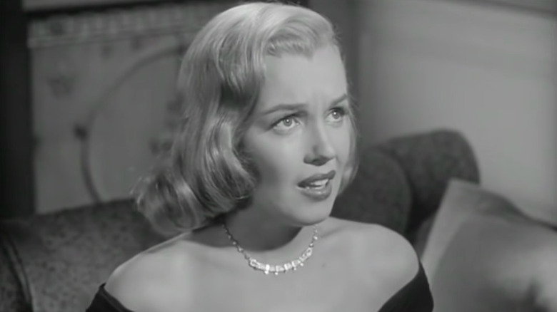 Monroe sitting on couch looking up at policeman 