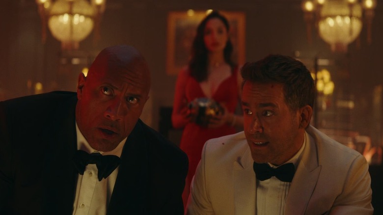 Ryan Reynolds looks at Dwayne Johnson while Gal Gadot stands in the background