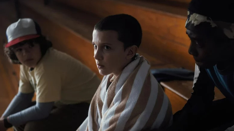 Dustin Henderson, Eleven, and Lucas Sinclair sit side by side on "Stranger Things" (2016-2025)