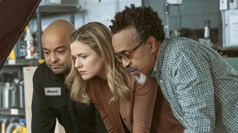 Colette, Armando, and Gregg gather around a car engine in "DMV"