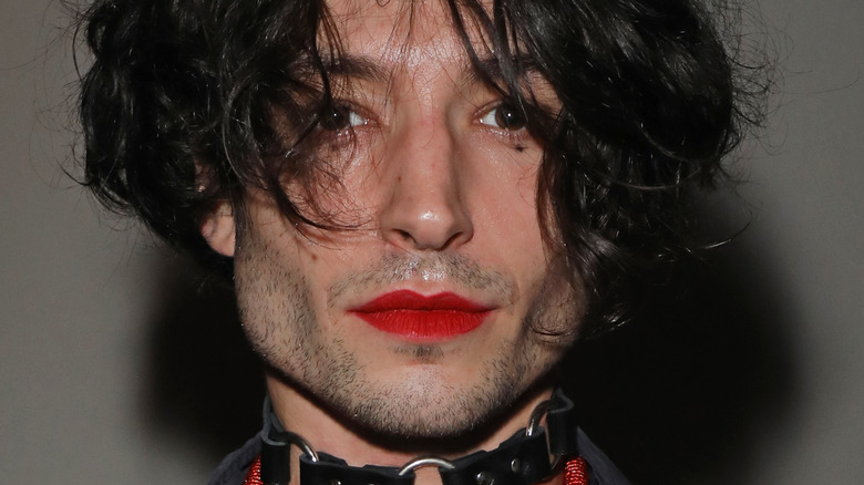 Ezra Miller with stubble, a black collar, and red lipstick