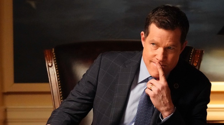 Dylan Walsh sitting at a desk with finger to his lips