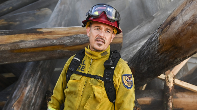 Manny standing exhausted among smoking logs in 