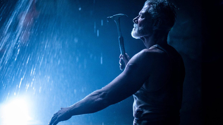 Blind Man stands under falling water with hammer