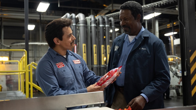 Two men stand in front of a production line of Cheetos