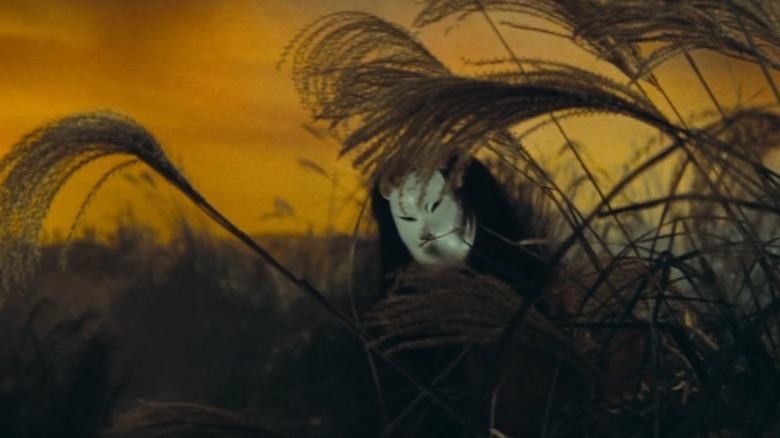 Person with fox max standing behind vegetation in The Mad Fox