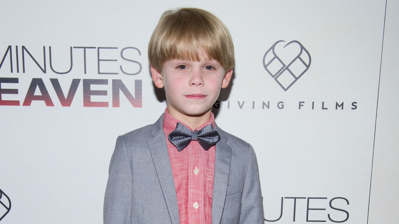 Hudson Meek en una blazer gris, una camisa roja y una mariposa