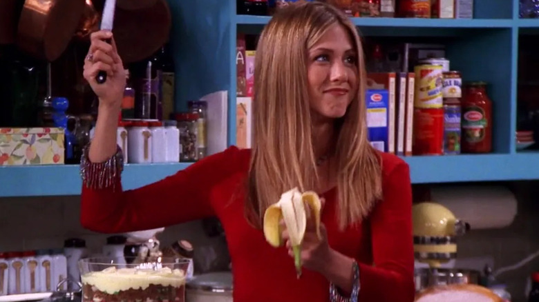 Rachel standing in her apartment's kitchen, with knife raised and a banana in hand in Friends