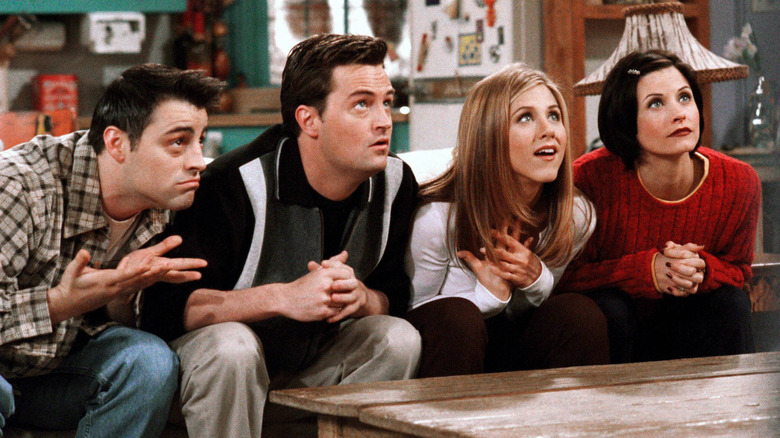 Joey, Chandler, Rachel, and Monica sitting on Monica's couch, looking up eagerly on Friends