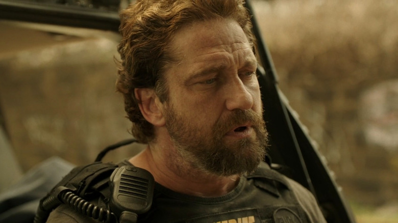 Nick O'Brien leaning against a cop cruiser in Den of Thieves