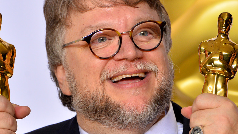 Guillermo Del Toro smiling and holding Oscars