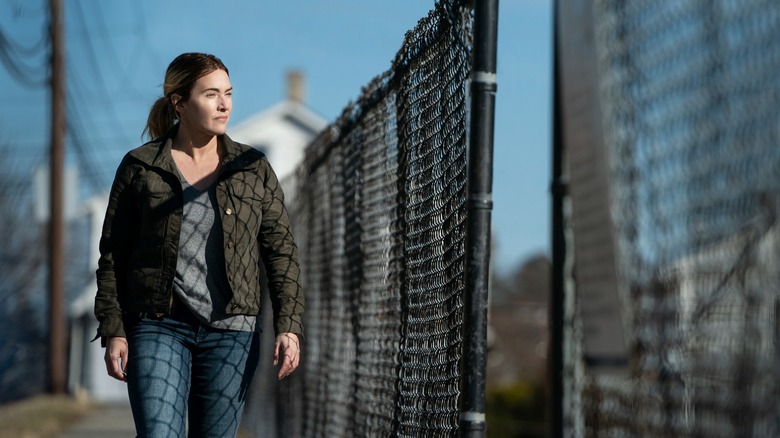 Detective Mare Sheehan walking by fence in Mare of Easttown (2021)