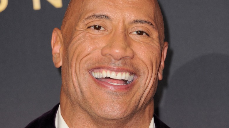 Dwayne Johnson smiling in front of a slate background