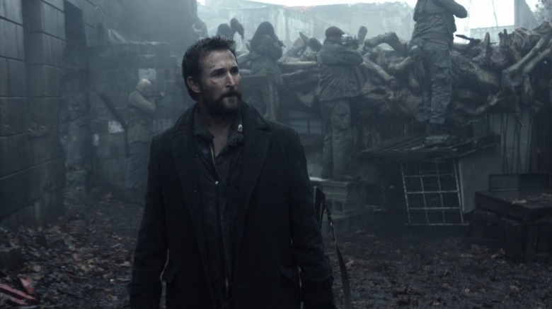 Tom on Falling Skies, standing in front of a wall made from alien bodies