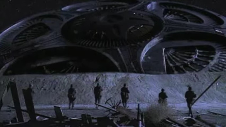 Military guys in silhouette walking toward a giant downed alien craft, from Taken