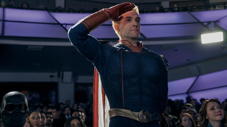 Homelander saluant quelque chose hors caméra alors qu'il est entouré d'un grand auditorium rempli de monde