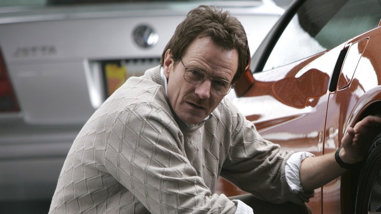 Walter White kneeling beside a car 