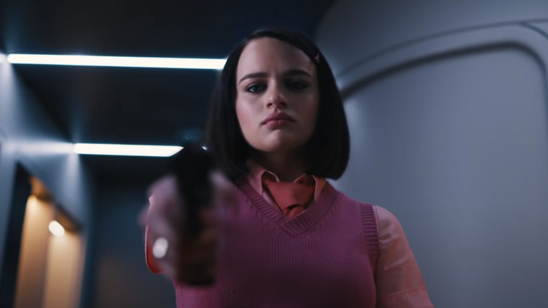 Joey King in a pink outfit aims a pistol