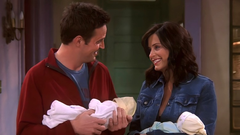 Chandler and Monica smiling while holding babies