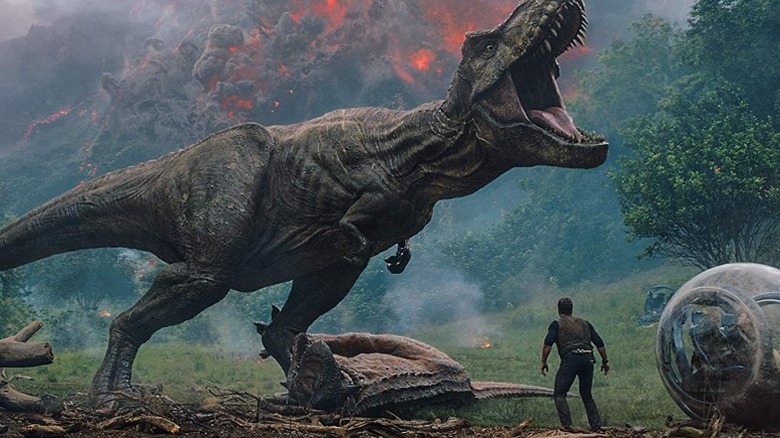 Owen Grady (Chris Pratt) stands under a T-rex as a volcano erupts in Jurassic World: Fallen Kingdom (2018)