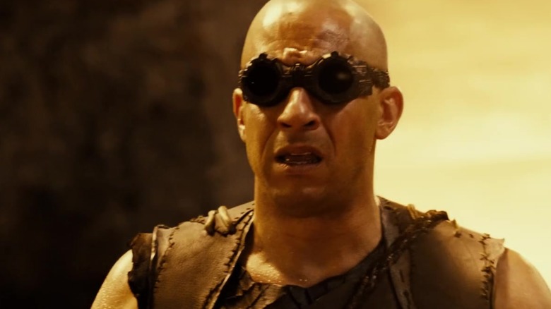 Riddick wearing goggles and grimacing in Riddick (2013)