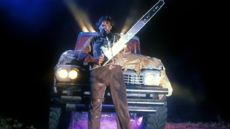Leatherface holding a chainsaw in front of a truck in "Leatherface: The Texas Chainsaw Massacre III."