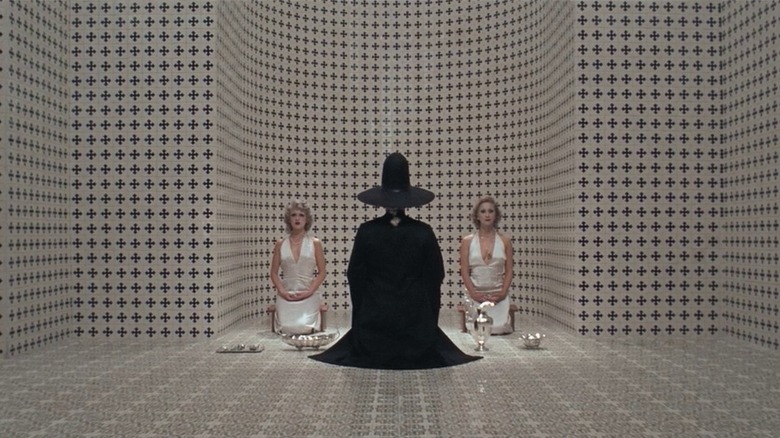 Two women in white sitting on either side of black robed figure
