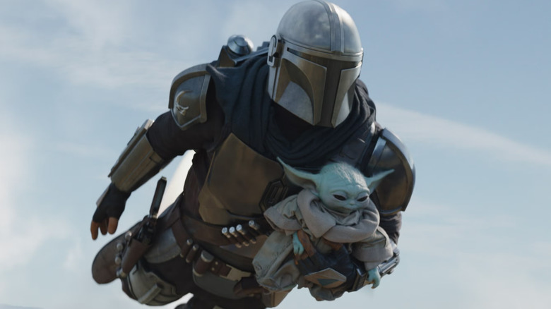 Din Djarin carrying Grogu as he flies in The Mandalorian and Grogu