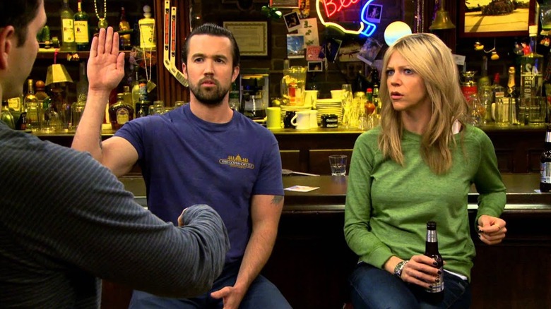 Mac raises his hand beside Dee in the bar in "It's Always Sunny in Philadelphia"