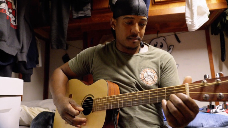 Jacob Hutchins playing guitar next to bed