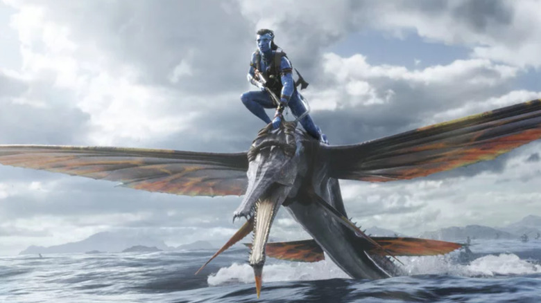 Jake Sully riding a water creature and holding a gun