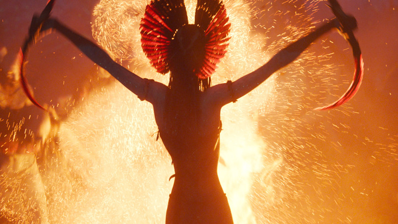 Varang raising her sickle blades in front of a raging bonfire in Avatar: Fire and Ash