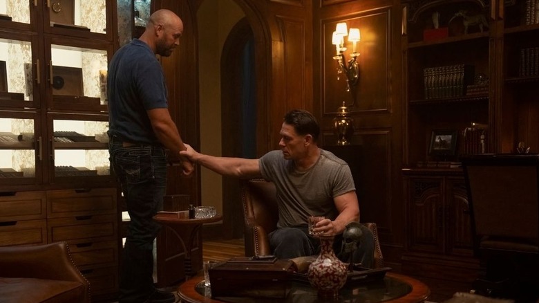 Peacemaker sitting in the library grasping Keith's wrist