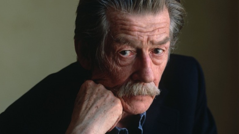 John Hurt looking at the camera with his head on his hand