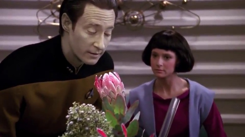 Data smells a flower while Lal sits behind him in Star Trek: The Next Generation