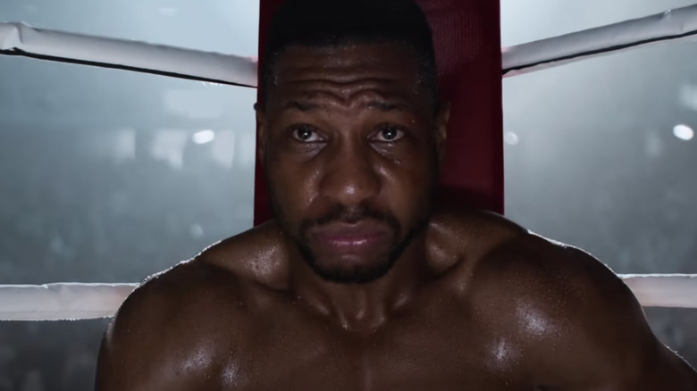 Jonathan Majors in Creed III shirtless sitting down in boxing ring looking sad