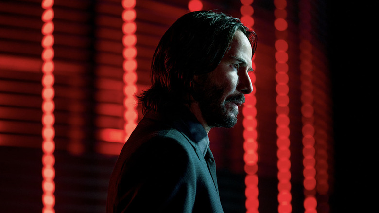 John Wick standing in front of neon red lights
