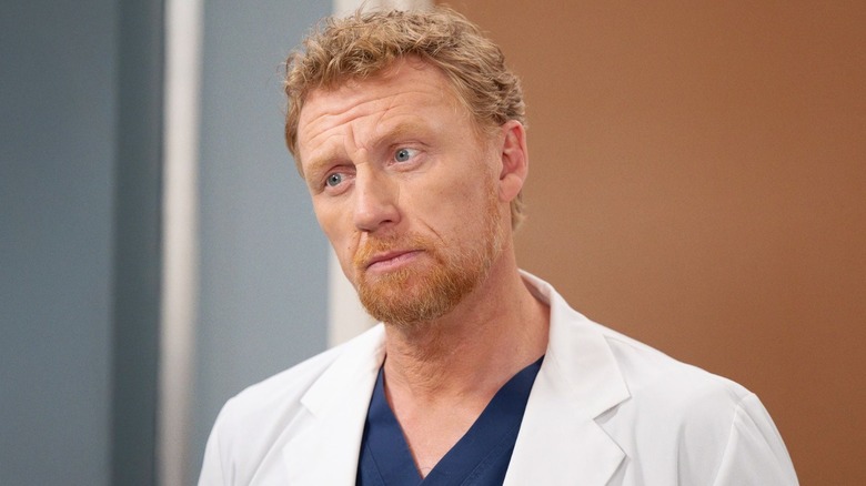 Owen looking concerned in a white coat and scrubs on Grey's Anatomy