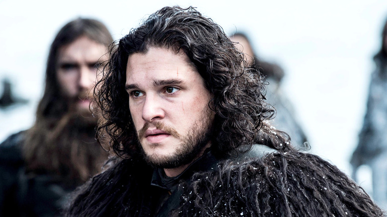 Jon Snow with long hair wearing black cloak
