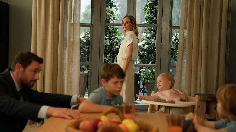 Jess standing at the window while her family sits at the table